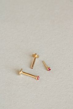 two gold screws are laying on a white surface and one has a red stone