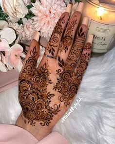 a woman's hand with henna on it next to some flowers and a candle