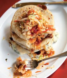 a plate topped with three tortillas covered in shredded cheese and toppings next to a fork