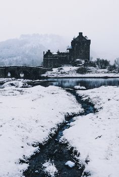 a small stream running through a snow covered field next to a castle in the distance