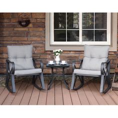 two chairs and a table sitting on a porch next to a brick wall with windows