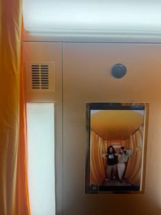 two people are standing in a room with yellow curtains on the wall and one person is taking a selfie