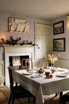 a dining room table set for two with plates and glasses on it, in front of a fireplace