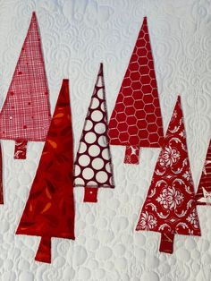 red and white christmas trees are hanging on the wall next to quilted tablecloth