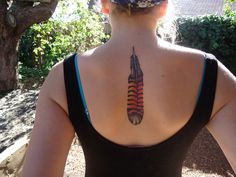 a woman with a tattoo on her back is looking at the trees and bushes behind her