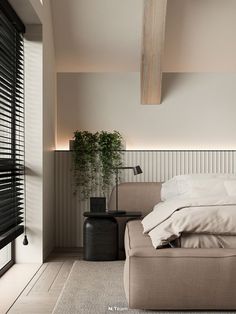 a large bed sitting under a window next to a wooden table and plant in a room