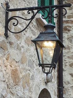 an old fashioned street light hanging from the side of a stone building with green shutters