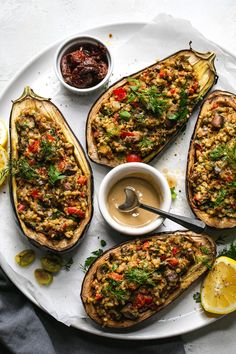 baked stuffed eggplant on a white plate with dipping sauce and lemon wedges