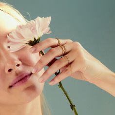 a woman holding a flower in front of her face and touching it with her hand