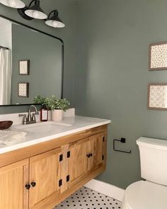 a white toilet sitting under a bathroom mirror next to a sink with a wooden cabinet