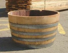 a large wooden barrel sitting in the middle of a parking lot next to stacks of lumber