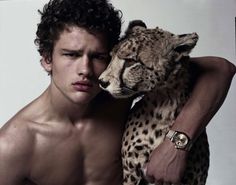 a shirtless man holding a cheetah in front of his chest and arm