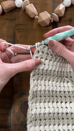 two hands are crocheting together to make a knitted bag on a wooden table