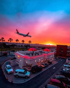 an airplane is flying over a parking lot at sunset with cars parked in the lot