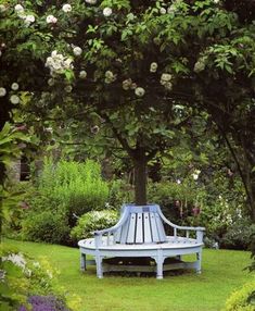 a blue bench sitting in the middle of a lush green park filled with lots of flowers