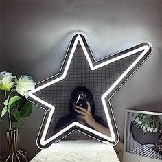 a woman taking a selfie in front of a star shaped neon sign with flowers