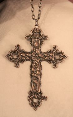 This goldtone necklace features a mid-to-large-sized pectoral cross pendant with swirled metal beaded fleur de lis accents on the ends of the arms.  The body shines with dogwood flowers - a symbol of new and everlasting life.  The reverse has a shiny finish and it measures 2 1/8 inches wide and 3 inches long.  The chain is 24 inches and closes with a safety catch Bronze Cross Bohemian Necklace, Vintage Metal Crucifix Cross Necklace, Bronze Bohemian Cross Necklace, Bohemian Bronze Cross Necklace, Ornate Cross Necklace With Intricate Design, Antique Cross Necklace With Large Pendant, Antique Metal Cross Necklace, Vintage Cross Necklace With Antique Finish, Antique Bronze Cross Necklace