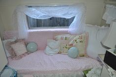 a pink day bed with white curtains and pillows on top of it in front of a window