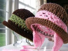 two crocheted hats sitting on top of a table next to a glass vase