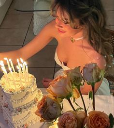 a woman sitting in front of a cake with lit candles on it and flowers next to the cake