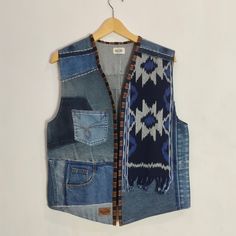 a denim vest hanging on a wooden hanger next to a white wall with a blue and black pattern