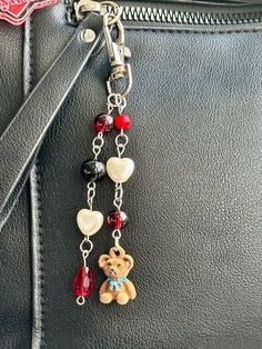 a teddy bear key chain hanging from a black leather purse with red, white and blue beads