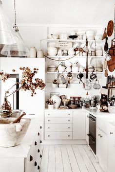 a white kitchen with lots of pots and pans hanging from the wall above the stove