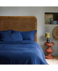 a bed with blue sheets and pillows next to a wicker headboard in a bedroom