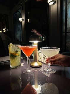 three cocktails are sitting on a table in a dimly lit room