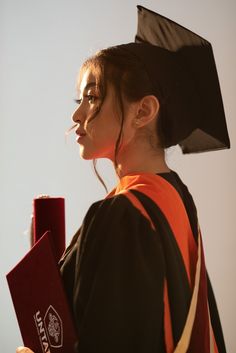 a woman wearing a black and orange graduation gown holding a red book in her right hand