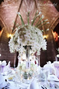 a tall vase filled with white flowers sitting on top of a table covered in plates and napkins