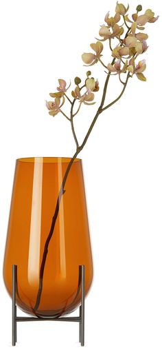 an orange vase with flowers in it sitting on a stand