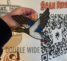 a person holding a bird shaped brooch in front of a wall with qr code on it