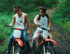 two young men sitting on dirt bikes in the woods