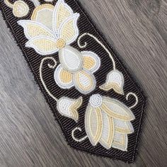 a black and yellow beaded ribbon with flowers on the side, sitting on a wooden surface