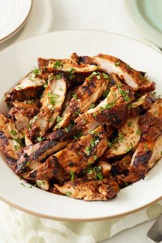 a white bowl filled with chicken and garnished with parsley