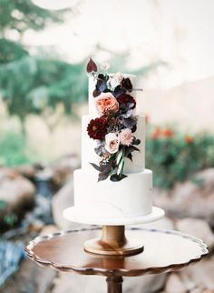 a three tiered white wedding cake with red and pink flowers on the top layer