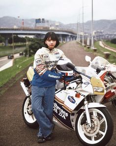 a person standing next to a motorcycle on a dirt road with mountains in the background