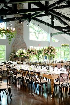 the tables are set up for an event with flowers and greenery hanging from the ceiling