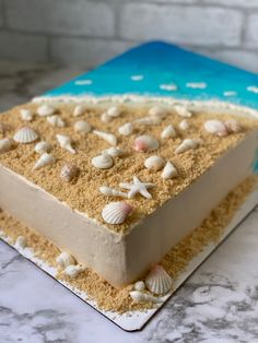 there is a cake that has shells on it and sand in the middle with blue water behind it