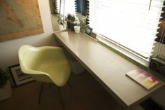 a yellow chair sitting in front of a window next to a wooden desk with a map on it