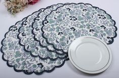 four placemats and two plates on a white tablecloth with flowers in the background