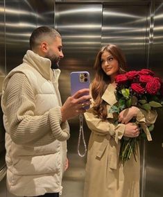 a man taking a selfie with a woman in front of an elevator holding flowers