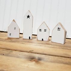 three small white wooden houses sitting on top of a wooden table next to a wall