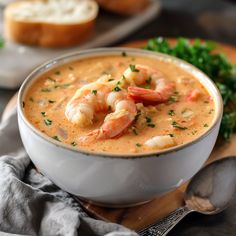 a bowl of soup with shrimp and bread in the background