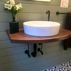 a white sink sitting on top of a wooden shelf next to a mirror and flowers