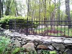 a stone wall and iron fence in the woods