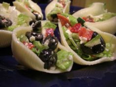 an assortment of pasta shells with olives, tomatoes and lettuce on them