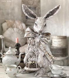 a rabbit statue sitting on top of a table next to tea cups and saucers