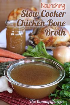 a bowl of chicken bone broth sitting on top of a table next to some vegetables